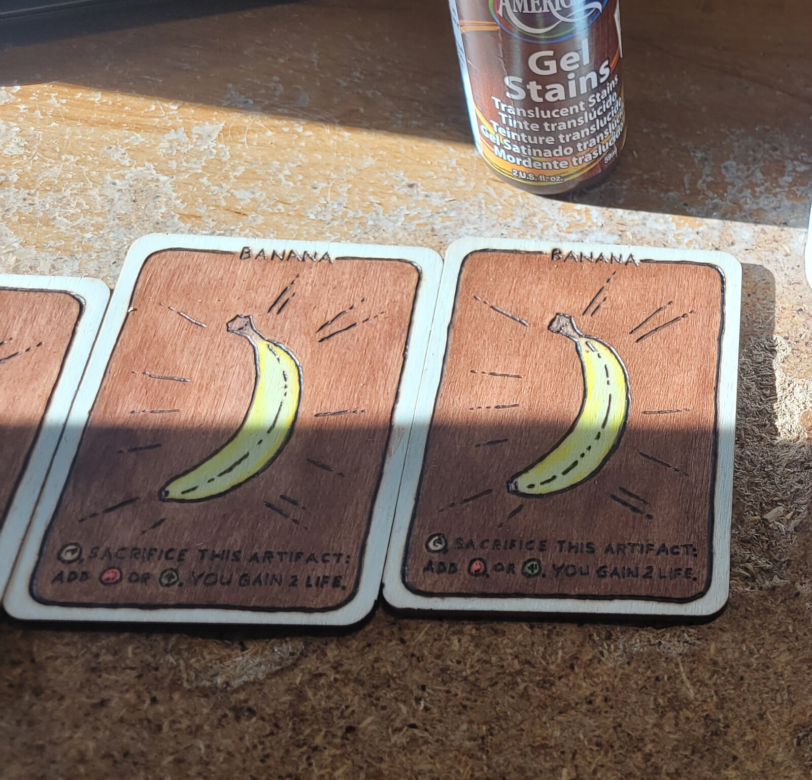 Client requested that Banana, and Mana Symbols be colored.
I colored them with a mixture of watercolor pencils and normal colored pencils. This allows a staining effect to the wood. Card background done in undiluted Maple, border and card back in walnut.